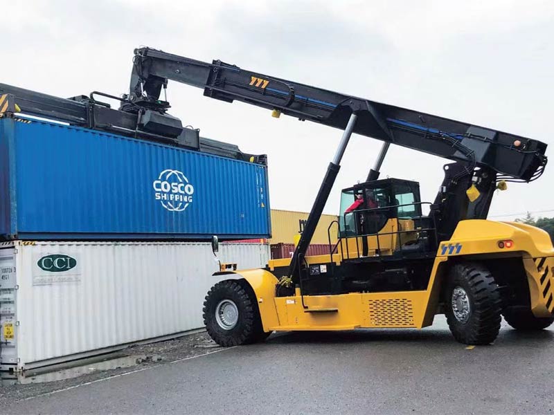 Reach stacker con brazo telescópico elevando un contenedor desde un camión de transporte.